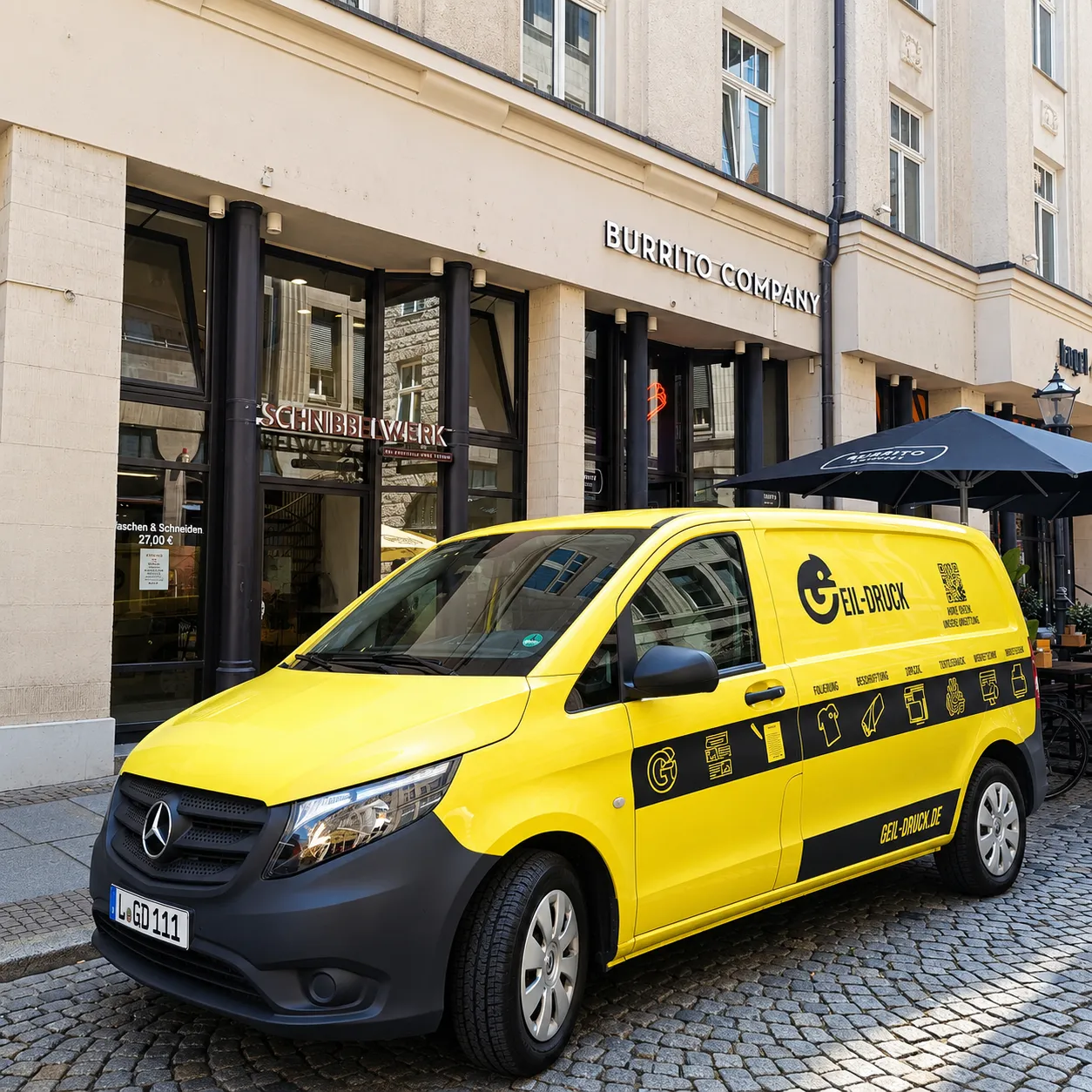 Gelber Geil-Druck-Firmentransporter vor dem beschrifteten Schnibbelwerk